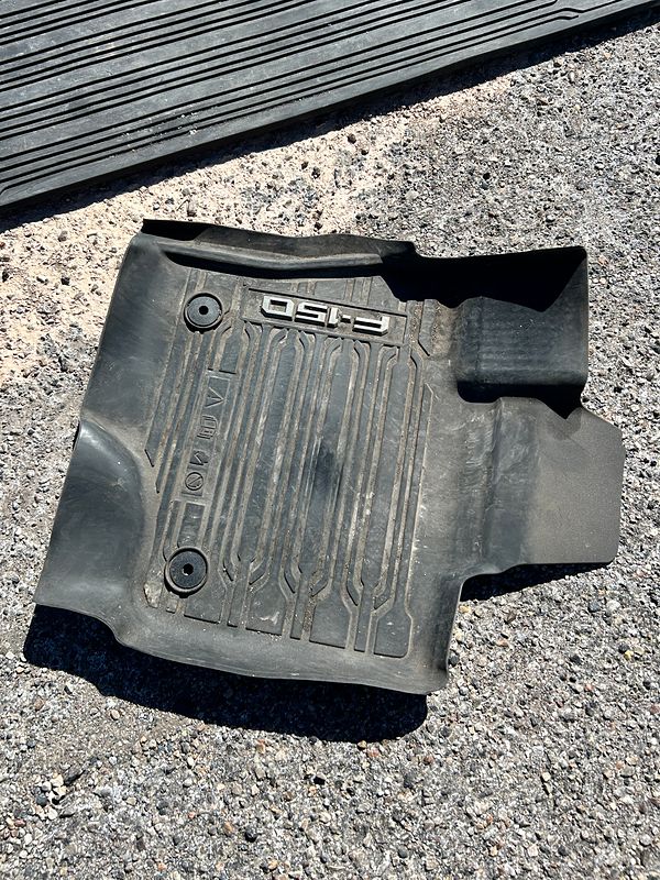 Before: the driver's floor mat from a Ford F-150, grey with dust, on the pavement