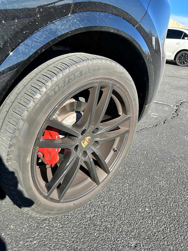 Before: a Porsche wheel coated grey with brake dust, its red brake caliper behind the spokes